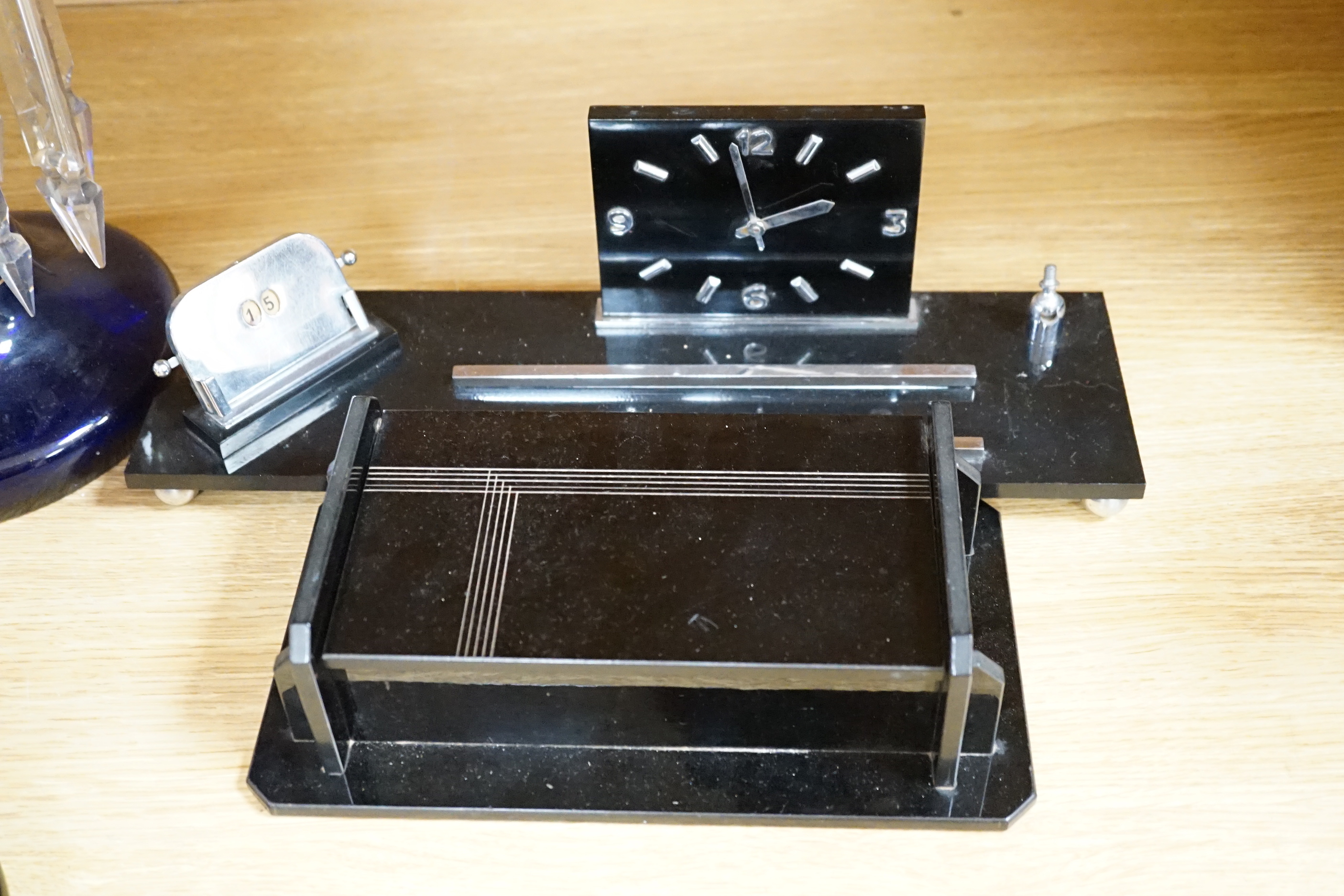 A black Bakelite box and similar clock desk stand, a faux marble clock, a marble clock, and a chrome box containing phenolic dominoes, desk stand 36cm wide (5)